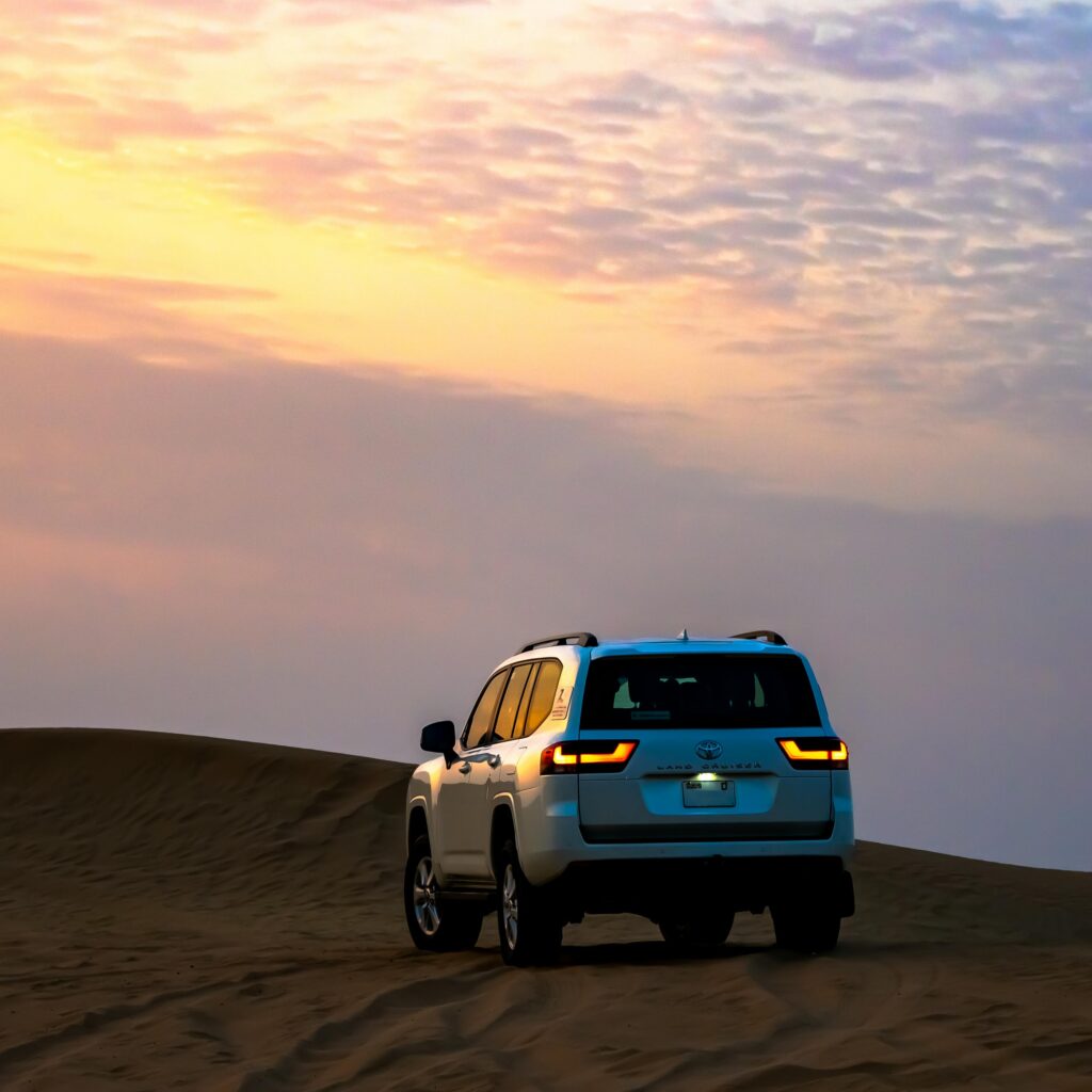 A vehicle traverses the sand dunes of Dubai's desert during a picturesque sunset.